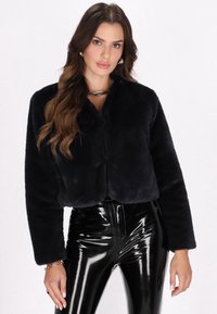 Jachetă scurtă din blană faux neagră, cu guler rotund, mâneci lungi și textură moale; asortată cu pantaloni negri strălucitori.