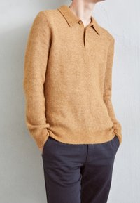 Stickad tröja i ljusbrun med en mjuk textur, med en krage och en avslappnad passform, matchad med mörka byxor.