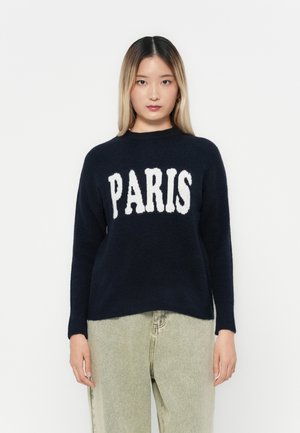 Pull marine avec "PARIS" en texte blanc sur le devant, col rond, manches longues, fabriqué dans une texture douce. Assorti à un pantalon de couleur claire.