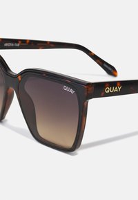 Tortoiseshell sunglasses with gradient lenses. Square shape, thick frames with gold "QUAY" lettering on the arms. Smooth plastic texture.