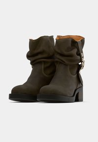 Bottines en cuir vert foncé au design décontracté, avec une bride à la cheville, des détails en métal argenté et un talon épais. Détails de surpiqûres contrastantes remarquables.