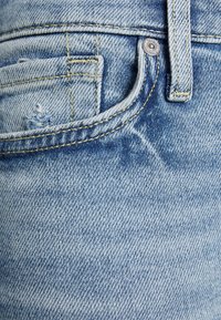 Jeans de denim azul claro con una textura desgastada, que presentan un bolsillo frontal, costuras visibles y un acento de botón de metal.