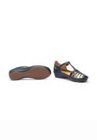 Zapatos de cuero negro con punta redondeada, diseño recortado y correas decorativas. Suela de goma marrón con un patrón de agarre texturizado.