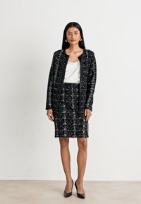 Ensemble de veste et jupe en tweed noir et blanc avec une forme structurée. Présente des accents en fils multicolores et un haut blanc lisse. Escarpins noirs.