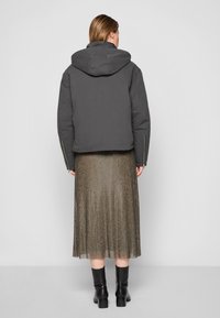 Dark gray, hooded puffer jacket with a cropped design. Paired with a pleated, metallic gold skirt and black ankle boots.