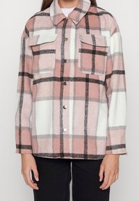 Ruudullinen ruutupaita pehmeästä, pörröisestä materiaalista. Värit vaaleanpunainen, valkoinen ja musta. Edessä kaksi rintataskua ja nepparikiinnitys.