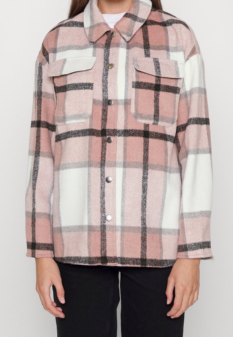 Ruudullinen ruutupaita pehmeästä, pörröisestä materiaalista. Värit vaaleanpunainen, valkoinen ja musta. Edessä kaksi rintataskua ja nepparikiinnitys.