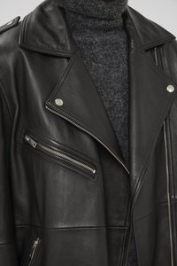 Black leather jacket with silver hardware, including zippers and snap buttons. Jacket features a notched collar and textured inner fabric.