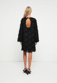 Μαύρο φόρεμα με μακριά μανίκια, υφαντό ύφασμα με φούντες και κυκλικό άνοιγμα στην πλάτη. Σχεδίαση μέσου μήκους, λεία επιφάνεια.