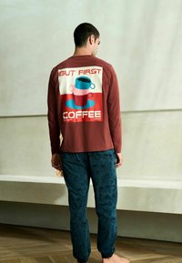 Tamsiai raudona ilgomis rankovėmis marškinėliai su puodelio grafiniu dizainu; tamsiai mėlynos kelnės su kavos tematikos raštais; laisvo kirpimo, minkšta medžiaga, kasdieniai drabužiai.