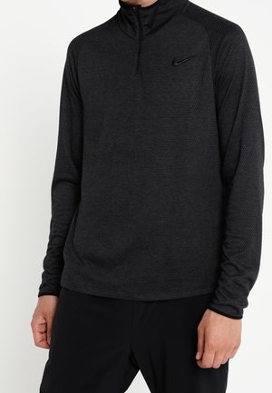 Mann trägt einen schwarzen Nike-Pullover mit langen Ärmeln, Reißverschluss am Kragen und strukturiertem Stoff, kombiniert mit schwarzer Hose.