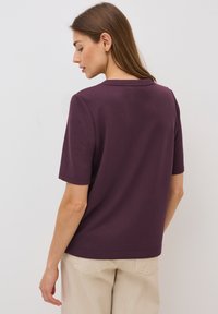 Korte mouwen top in donkerpaars stof met een ronde hals. De achterkant toont een eenvoudig ontwerp en een rechte zoom.