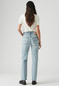 Jean taille haute bleu clair avec une coupe décontractée, dotés de poches arrière et d'une étiquette de marque. Porté avec un haut à manches courtes blanc.