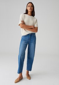 Maglione a maglia corto, color crema, abbinato a jeans blu a gamba dritta con vita alta e scarpe slip-on color nude, che mostrano un fit rilassato.