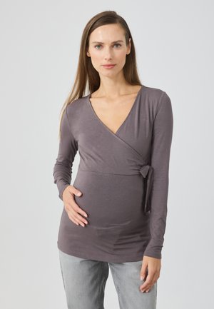 Langdurige mouw, wikkel-stijl zwangerschapsblouse van zachte, grijze stof met een strikaccent bij de taille, aansluitend rond de buik, gladde textuur.