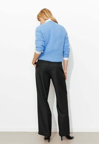 Pull en laine bleu clair, col de chemise blanc visible en dessous. Pantalon noir à jambes larges avec des rayures verticales discrètes. Chaussures noires à talons hauts.
