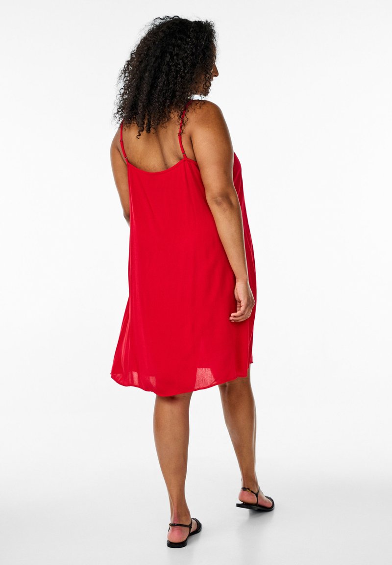 Rotes ärmelloses Kleid aus leichtem Stoff, mit lockerer Passform, dünnen Trägern und einem knielangen Saum. Flache Sandalen runden das Outfit ab.