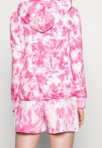 Set di abbigliamento da casa in tie-dye rosa, composto da una felpa con cappuccio a maniche lunghe e pantaloni corti coordinati. Tessuto morbido con diverse fantasie in rosa.
