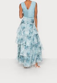 Robe superposée bleu clair avec un bodice en dentelle et un col en crête. La jupe présente un tissu fluide et semi-transparent avec un motif floral.
