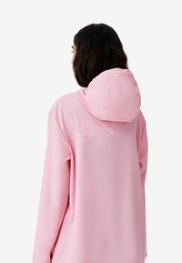 Rosafarbener Kapuzenpullover mit entspannter Passform, weicher Textur und Nahtdetails im oberen Rückenbereich. Die Kapuze ist abgerundet und festgenäht.
