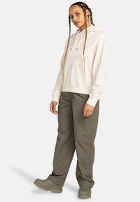 Beige hoodie with front pocket, drawstrings, paired with loose olive green pants and greenish boots. Smooth texture, casual fit.