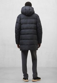 Czarna ocieplana parka z kapturem, posiadająca konstrukcję z przegrodami. Szare spodnie i czarne tenisówki uzupełniają strój. Prosty, funkcjonalny styl.