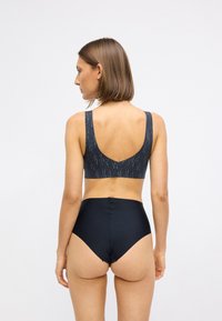 Sorte høj talje trusser parret med en mørkt mønstret bralette med brede stropper og scoop rygdesign i en glat stoftekstur.