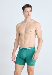 Zeleni bombažni bokserice s širokim elastčnim pasom, na katerem je bel Nike logotip. Prilagojen dizajn s gladko teksturo in dolžino do sredine stegna.