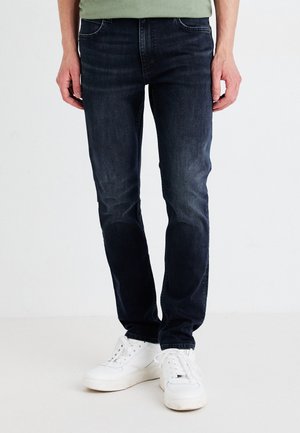 Mørkeblå denimjeans med slim fit, med fem lommer og subtil fading, kombinert med hvite joggesko. Glatt tekstur og klassisk design.