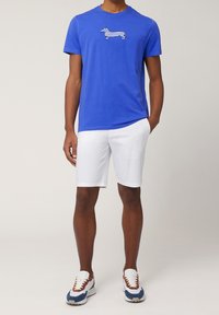 Blå bomullströja med en randig taxgrafik, ihop med vita shorts och sneakers med bruna detaljer.