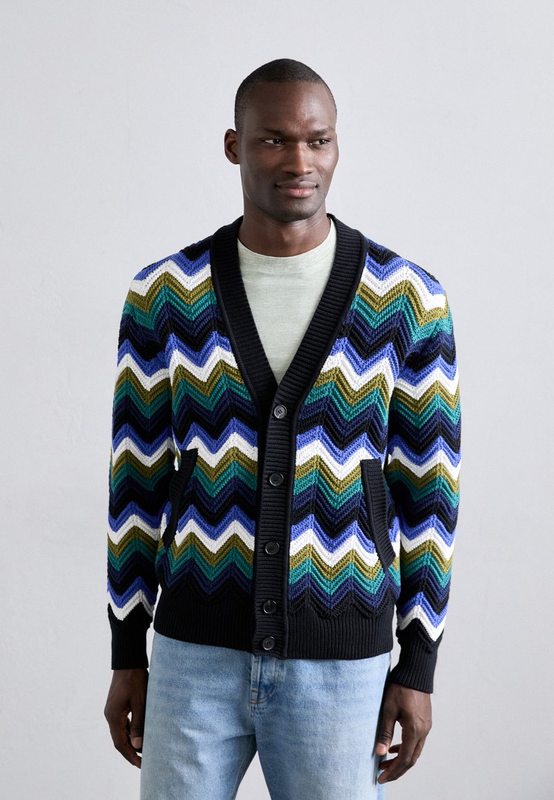 Cardigan tricotat în zigzag multicolor, prezentând nuanțe de verde, albastru, alb și negru, cu decolteu în V, închidere cu nasturi și două buzunare frontale.