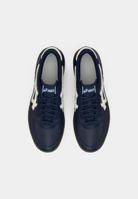 Tmavě modré sportovní boty s hladkým koženým svrškem, bílými akcenty, šněrováním a perforovaným detaily na špičce. Měkká podšívka a polstrovaná podešev.