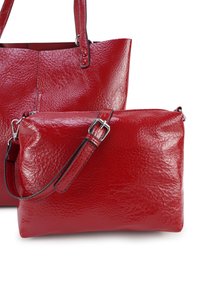 Twee textuurvolle rode leren handtassen met verstelbare banden, een grotere tote en een kleinere crossbody, tegen een witte achtergrond.