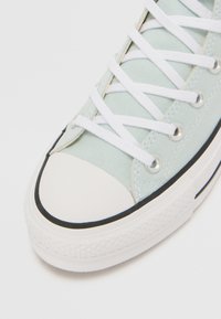 Ljusblå canvas-sneakers med vita snören, gummitåspets och svart kant. Har metalöglor och strukturerad såldesign.