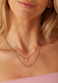 Colliers en argent à plusieurs couches avec un pendentif en forme de cœur et un pendentif "love", présentant une texture lisse et un design de chaîne délicat.