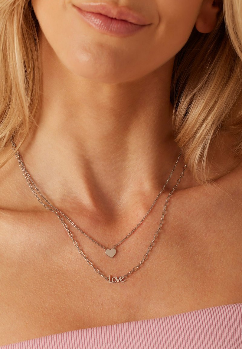 Colliers en argent à plusieurs couches avec un pendentif en forme de cœur et un pendentif "love", présentant une texture lisse et un design de chaîne délicat.