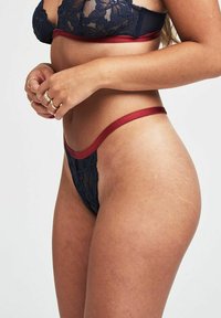 Kant lingerie set met een marineblauwe bh met een bloemenpatroon en een bijpassende thong met rode rand. Toont gladde stof en minimale bedekking.