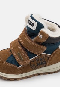 Brun mockaskinn och turkost textil ankelsko med två kardborreband, fuskpälsfoder och mönstrad logotyp på sidan. Har GORE-TEX-märke.