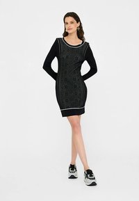Robe noire avec une texture à motif, manches longues, et bordure blanche au niveau de l'encolure et de l'ourlet. Portée avec des baskets noires et blanches.
