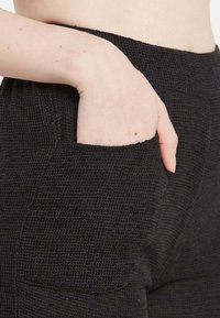 Črne h textured hlače z obsežnim stranskim žepom, tkanina iz prepletene zasnove v ohlapnem slogu za udobje in praktičnost.