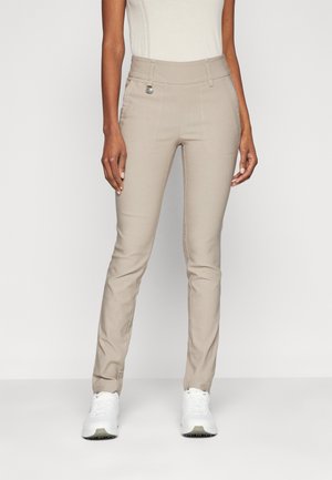 Beige, slim-fit pants with a high waistband, subtle stitching details, and a small metal accent near the waist, paired with white sneakers.
