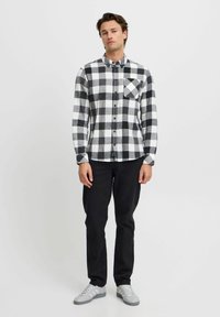 Zwart-wit geblokt flanellen shirt met lange mouwen, knoopsluiting en een voorkantzak. Draagt het met zwarte broek en grijze sneakers.