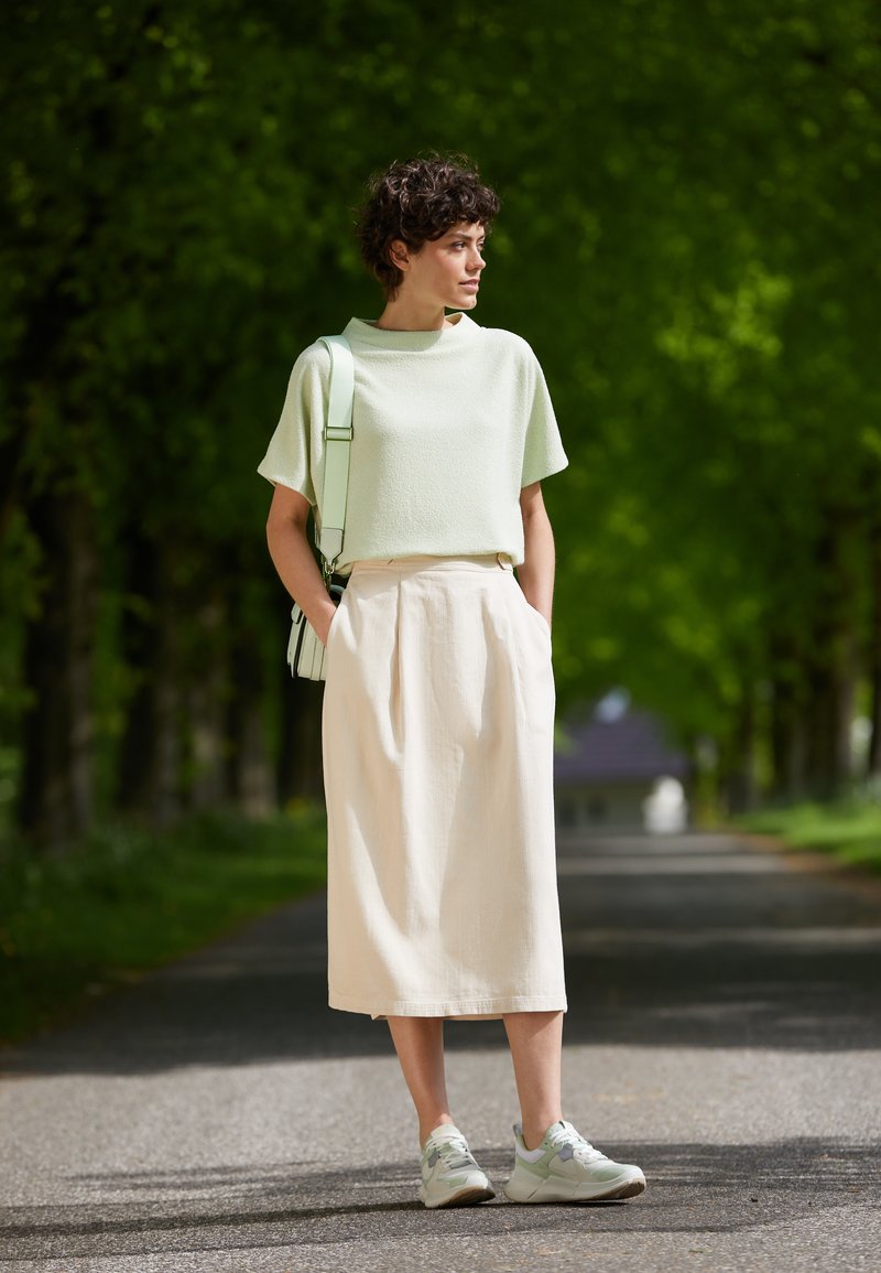 Top corto a maniche corte verde chiaro con texture, gonna midi crema con pence e sneakers verde menta. L'outfit è completato da una borsa a spalla verde chiaro.