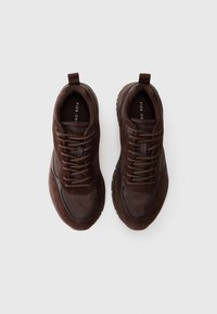 Brown sneakers featuring suede and mesh materials, rounded toe, thick rubber sole, and lace-up design with a pull tab on the tongue.