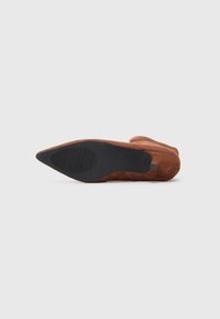 Stivaletto in suede marrone con punta affusolata, suola in gomma nera e sottili accenti plissettati sui lati. Texture liscia nel complesso.