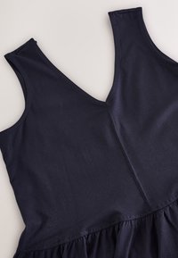 Mörkblå ärmlös klänning med V-ringning, tillverkad av mjukt tyg. Har rynkad textur vid fållen och slät finish.