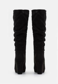 Botas de ante negras, hasta la rodilla, con un diseño arrugado, que cuentan con un tacón alto grueso para mayor soporte y una superficie suave y texturizada.