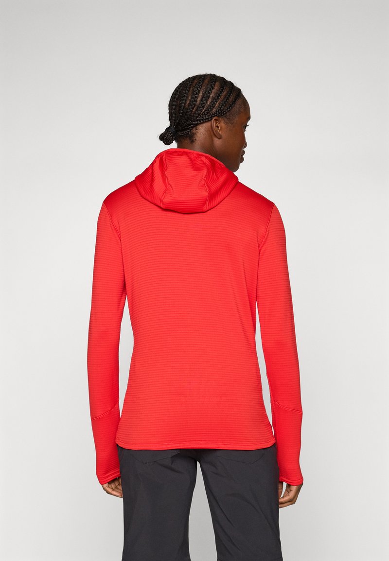 Czerwona bluza z długim rękawem i kapturem, z ukośnymi szwami i teksturowaną powierzchnią. Posiada dopasowany kaptur oraz otwory na kciuki przy mankietach, umieszczona na jednolitym tle.