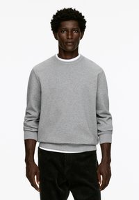 Gray sweatshirt with a crew neckline, long sleeves, and ribbed cuffs. Worn over a white T-shirt and paired with dark corduroy pants.