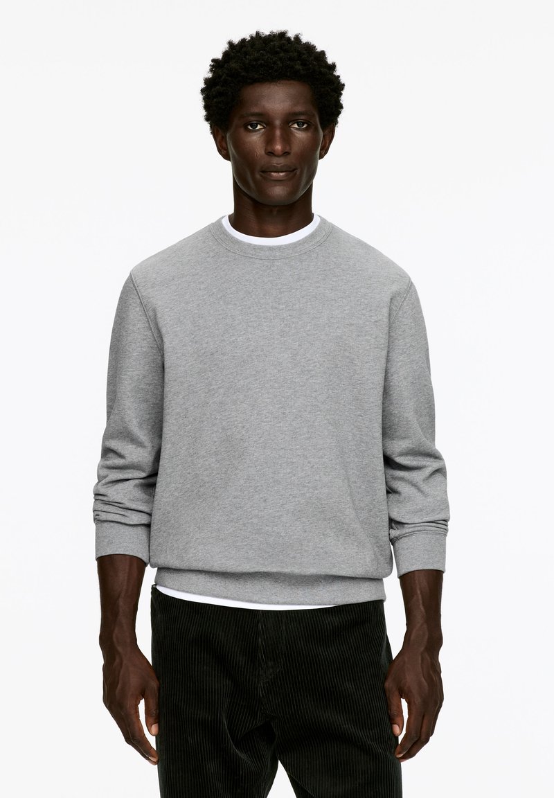 Gray sweatshirt with a crew neckline, long sleeves, and ribbed cuffs. Worn over a white T-shirt and paired with dark corduroy pants.